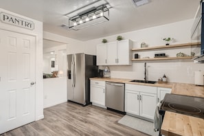A modern kitchen with white cabinets, a stainless steel refrigerator, a dishwasher, and a wooden countertop. - Relaxing 3BR w/ Waffle Bar•Lackland BMT•Seaworld! (San Antonio)