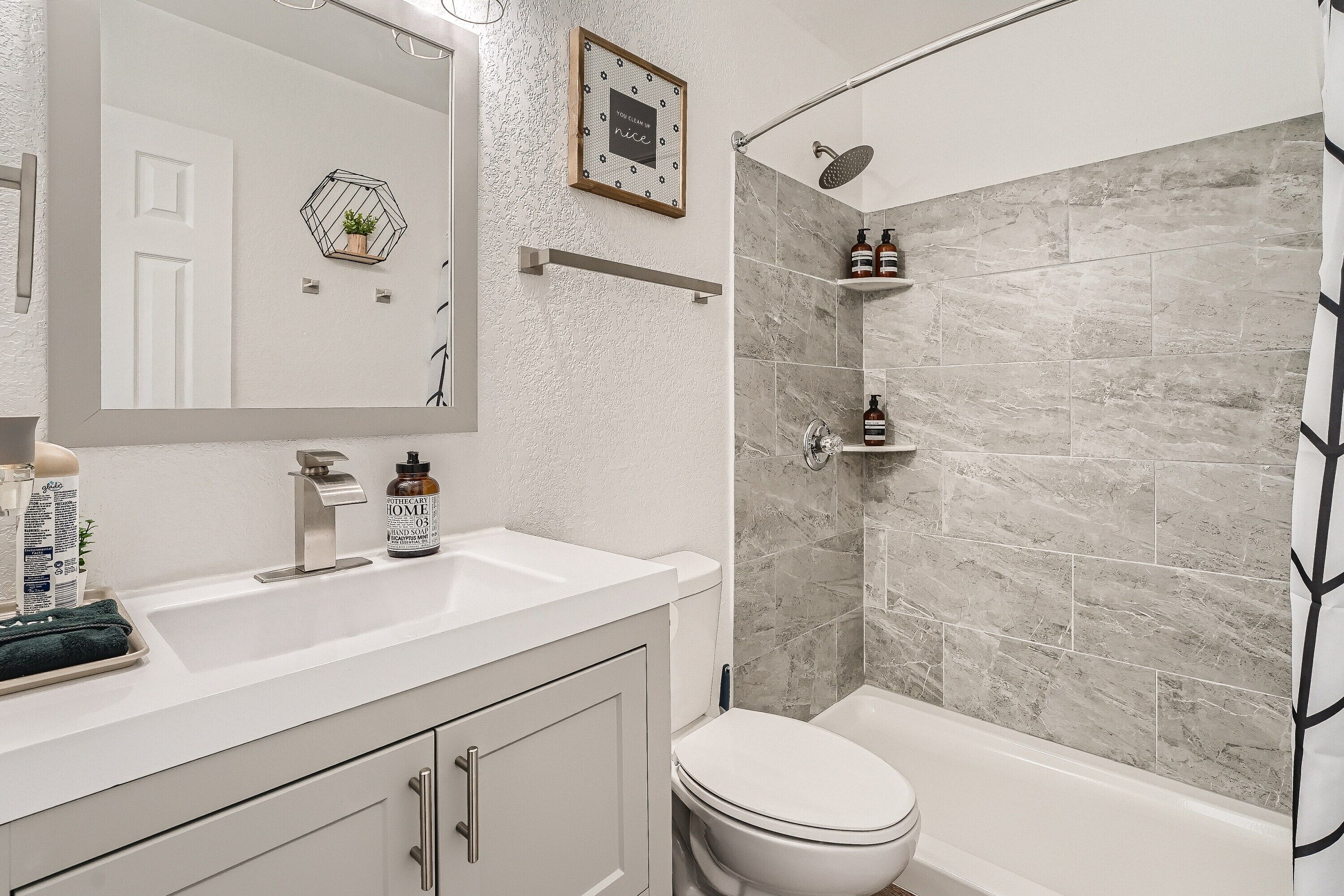 Un baño con un lavabo blanco, un inodoro y una zona de ducha con azulejos grises.
