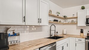 A modern kitchen with white cabinets, a wooden countertop, a dishwasher, a sink, and a coffee maker. - Relaxing 3BR w/ Waffle Bar•Lackland BMT•Seaworld (San Antonio)