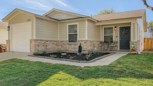 A single-story house with a front porch, a garage, and a landscaped front yard. - Relaxing 3BR w/ Waffle Bar•Lackland BMT•Seaworld (San Antonio)