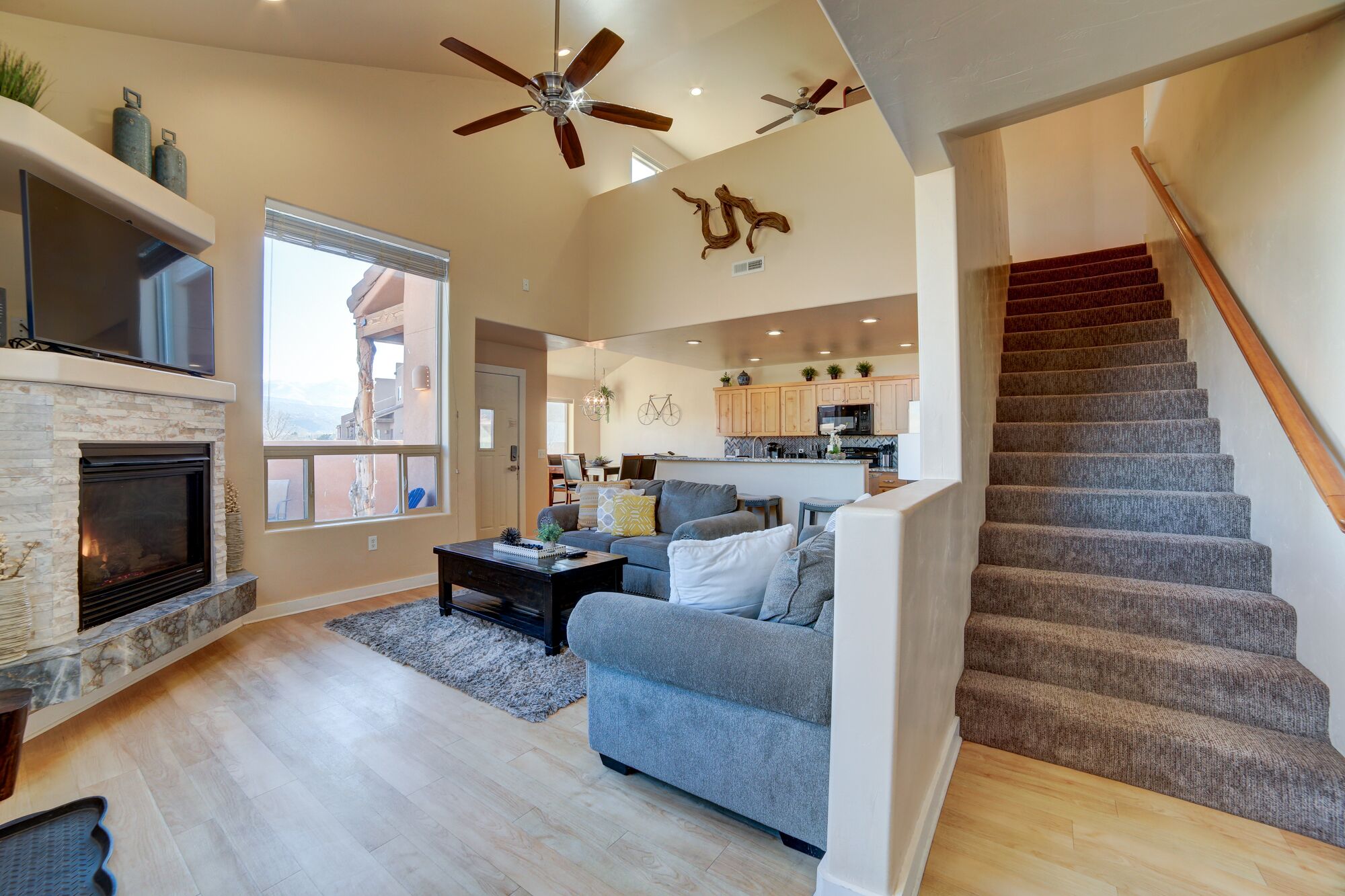 A spacious living area with a fireplace, a grey sofa, and a staircase leading to the upper floor.