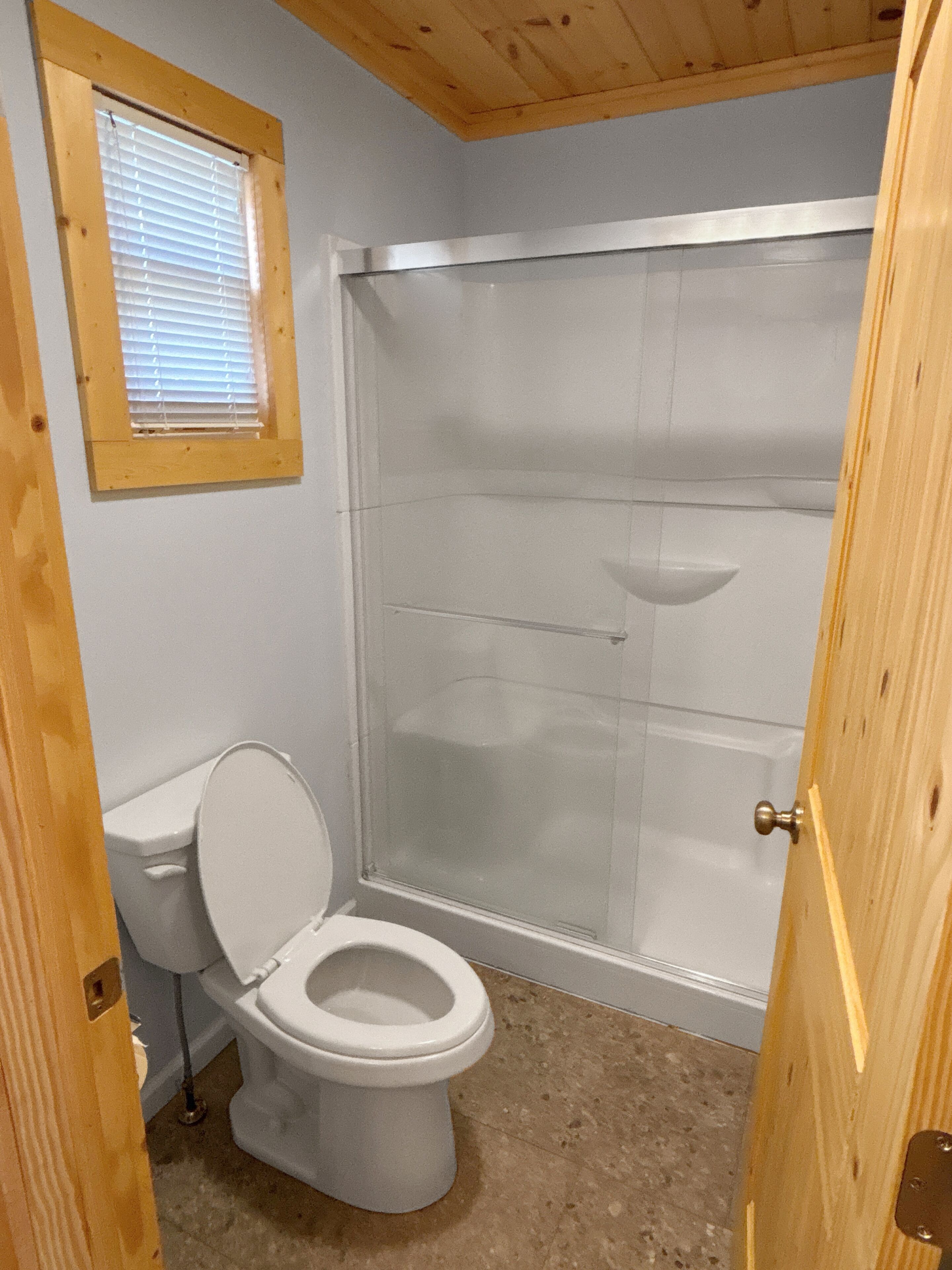 A bathroom with a toilet, a shower, and a window.