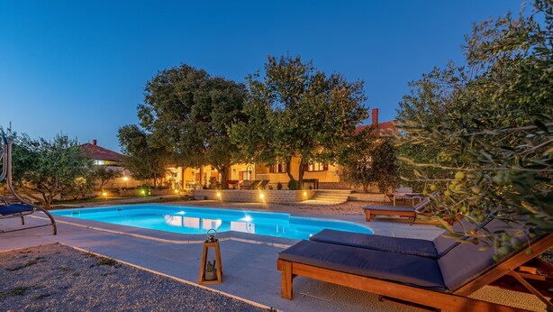 A swimming pool with lounge chairs and a pergola, surrounded by trees and a building with lights. - Holiday Home Apios - Three Bedroom Holiday Home with Swimming Pool (Benkovac)