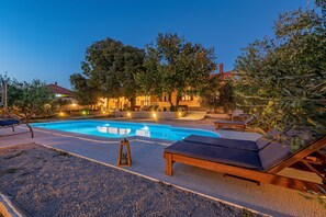 A swimming pool with lounge chairs and a pergola, surrounded by trees and a building with lights. - Holiday Home Apios - Three Bedroom Holiday Home with Swimming Pool (Benkovac)
