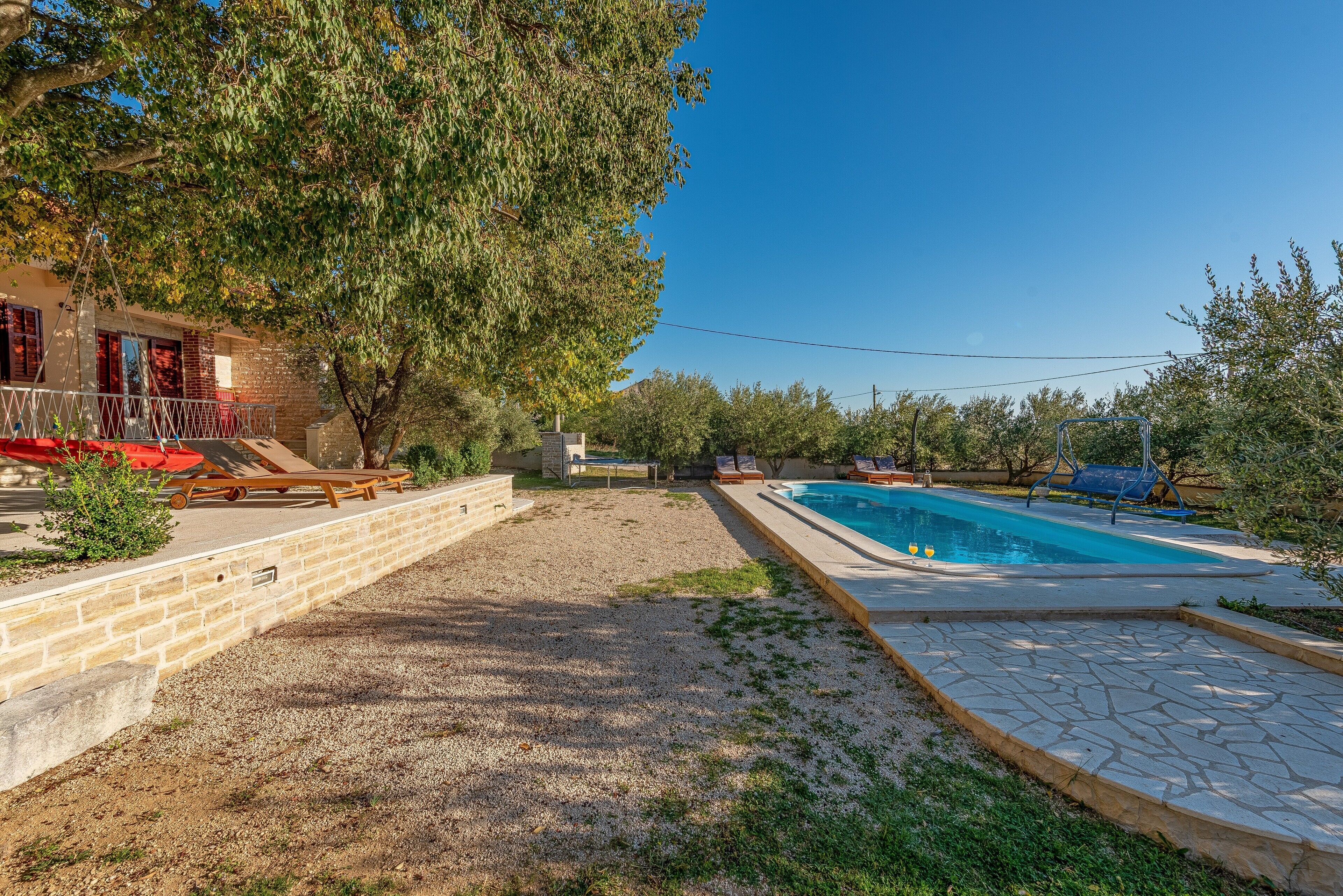 A backyard with a swimming pool, a patio area with lounge chairs, and a stone wall.