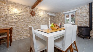A dining area with a stone wall, a wooden table, white chairs, and a black stove. - Holiday Home Apios - Three Bedroom Holiday Home with Swimming Pool (Benkovac)