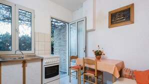 Een kleine keuken met een fornuis, wastafel en een eethoek met een tafel en stoelen.