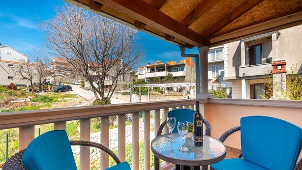 Een balkon met rieten stoelen en een tafel, met uitzicht op een woonwijk met gebouwen en een boom.