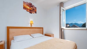 Een hotelkamer met een bed, een nachtkastje, een lamp, een raam met uitzicht op de bergen en een kunstwerk aan de muur.