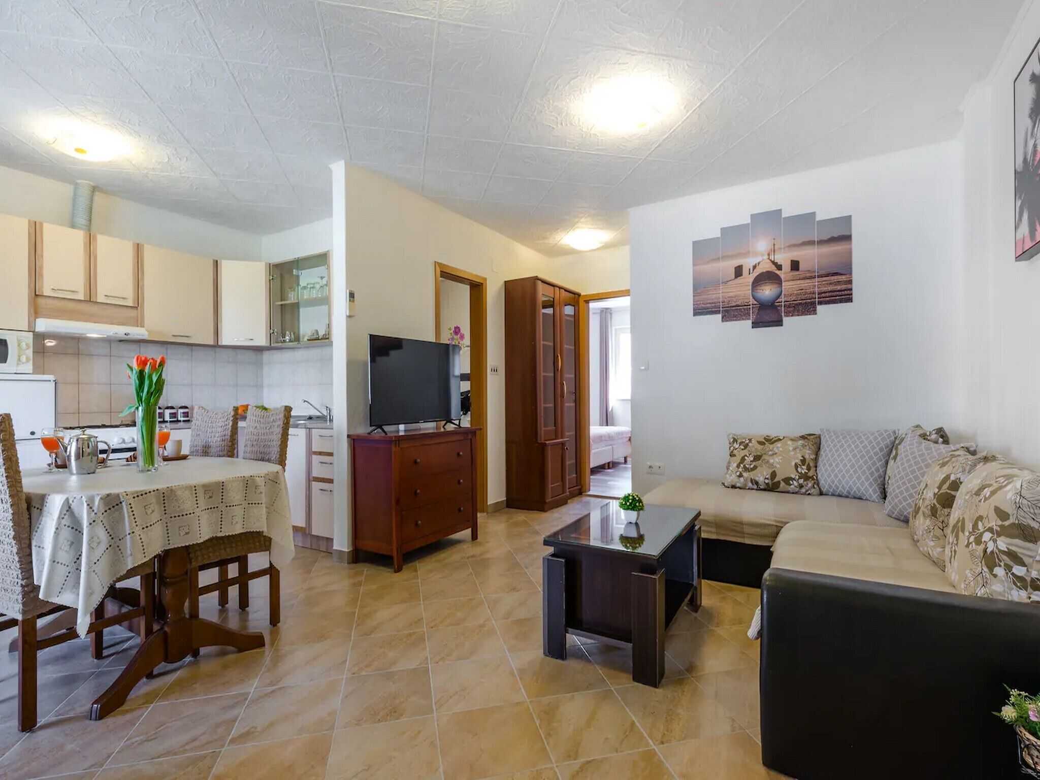 Una sala de estar con sofá, una mesa de centro y un televisor. Se observa una mesa de comedor con sillas y una zona de cocina al fondo.