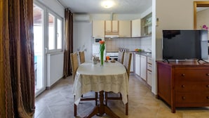Een eetgedeelte met een ronde tafel, stoelen, een televisie en een keuken op de achtergrond.