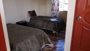 Ein Zimmer mit zwei Betten, einem Fenster mit Vorhängen und einem Fliesenboden.
