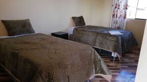 Ein Hotelzimmer mit zwei Betten, jeweils mit gemustertem Bettbezug und Kissen. Der Raum hat einen Fliesenboden und ein Fenster mit Vorhängen.