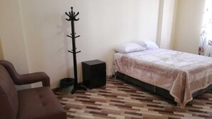Ein Zimmer mit einem Bett, einem Sessel, einem Kleiderhaken und einem kleinen schwarzen Schrank.