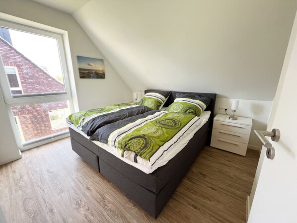 A bedroom with a bed, a nightstand, a drawer unit, and a window with a view of a brick building.