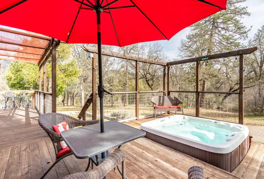 A wooden deck with a hot tub, wicker chairs, and a red umbrella.