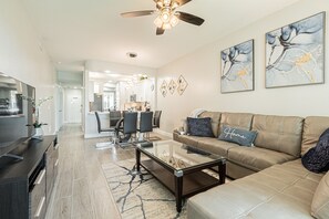 A modern living room with a leather sofa, a glass coffee table, and a dining area in the background.