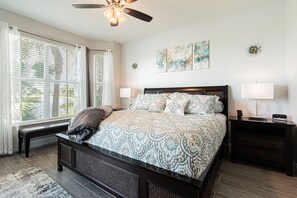 A bedroom with a large bed, a ceiling fan, a bench by the window, and artwork on the wall.