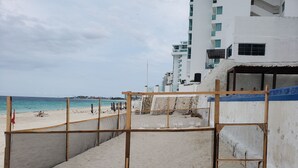 Ein Strand mit einer Holzkonstruktion, einem Sandweg und einem Gebäude im Hintergrund.