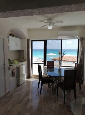 A dining area with a table and chairs, a ceiling fan, and a view of the beach through large windows. - Amazing Studio by the beach (Cancún)