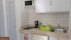 A compact kitchen with white cabinets, a microwave, a sink, and a small refrigerator. - Amazing Studio by the beach (Cancún)