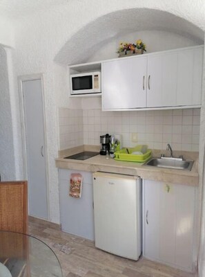 Compact kitchen with microwave, refrigerator, and sink, featuring a tiled backsplash and single light fixture.