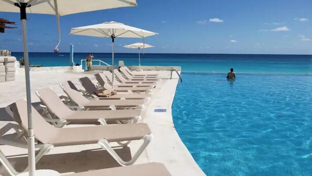 Un espace aménagé au bord de la piscine, avec des chaises longues et des parasols, offrant une vue sur un océan d’un bleu limpide.