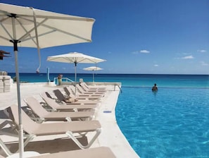 A poolside area with lounge chairs and umbrellas, overlooking a clear blue ocean. - Beachfront with amazing view (Cancún)