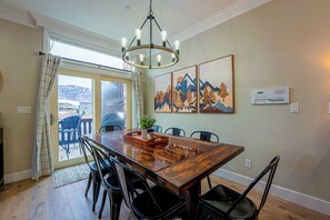 A dining area with a wooden table, black chairs, a chandelier, and mountain-themed artwork on the wall. - Heaven’s Gate LS48 | Ski Retreat | Hot Tub & Views (Huntsville)