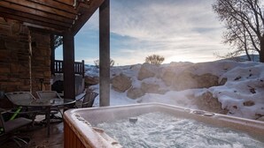 Un jacuzzi en un espacio al aire libre con paredes de piedra y vistas a colinas nevadas.