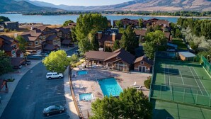 Zona residencial con casas, una piscina, canchas de tenis y un lago con montañas al fondo.