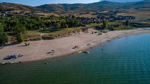 Vista aérea de una zona costera con playa arenosa, barcos y colinas con edificios al fondo.