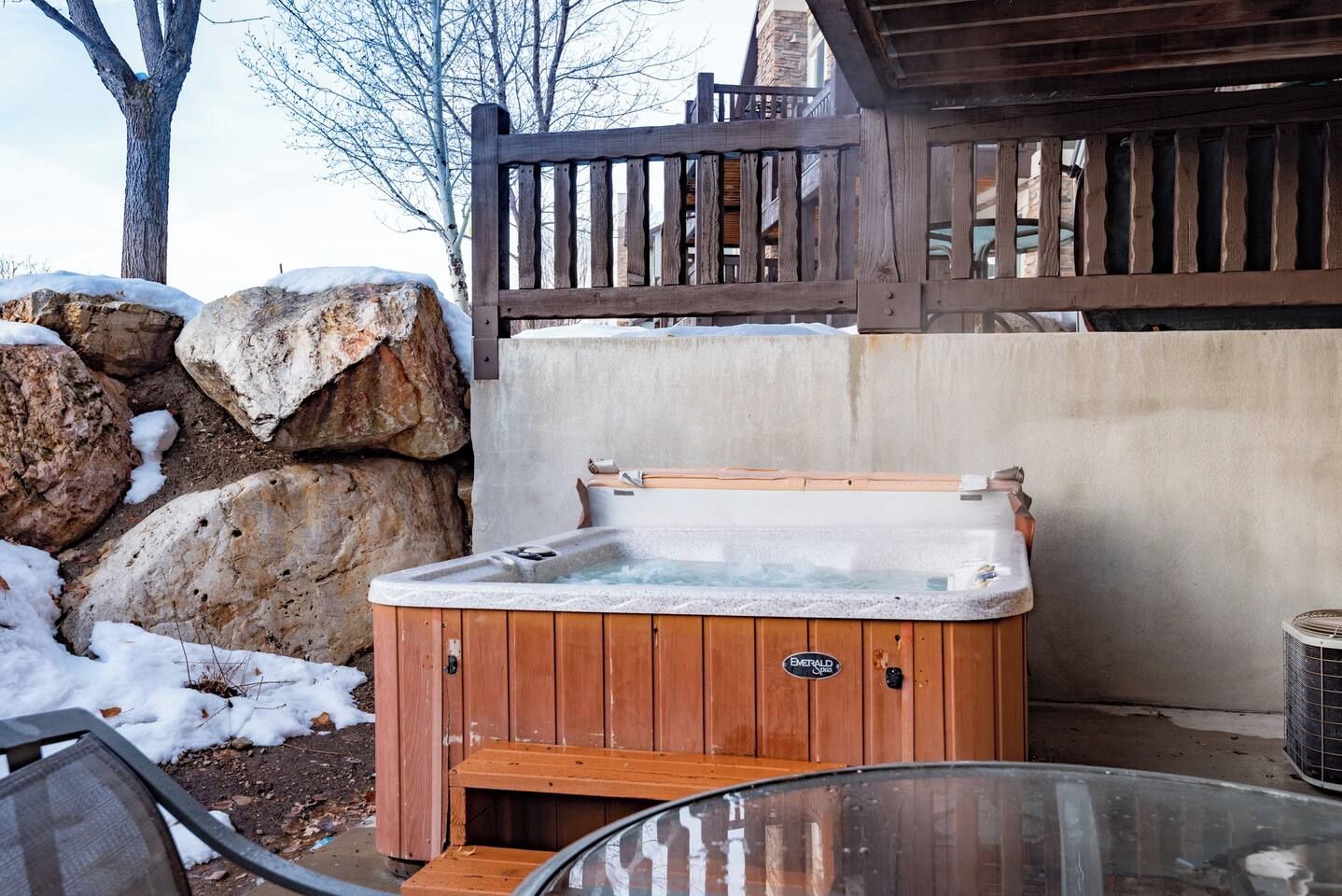 Una vasca idromassaggio in un ambiente esterno con un decking in legno e un muro in pietra.