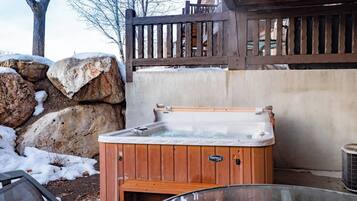 Una vasca idromassaggio in un ambiente esterno con un decking in legno e un muro in pietra.