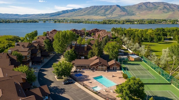 Zona residencial con casas, piscina, canchas de tenis y un lago con montañas al fondo.