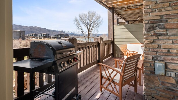 Une terrasse extérieure avec un barbecue, des chaises en bois et une vue sur des bâtiments et des montagnes lointains.
