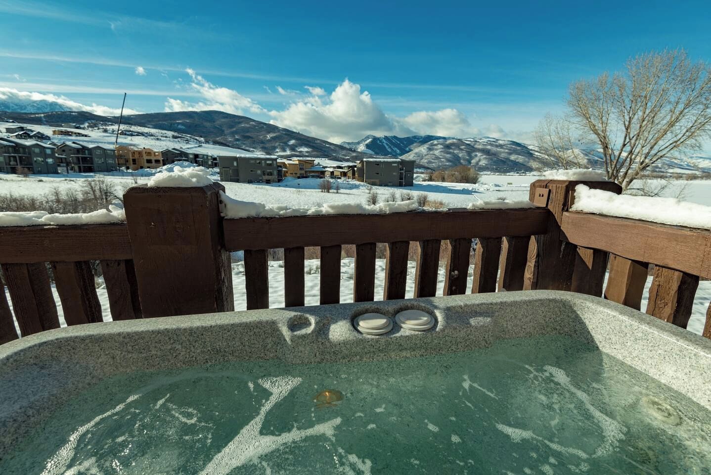 Un bain à remous avec vue sur des bâtiments enneigés et des montagnes en arrière-plan.