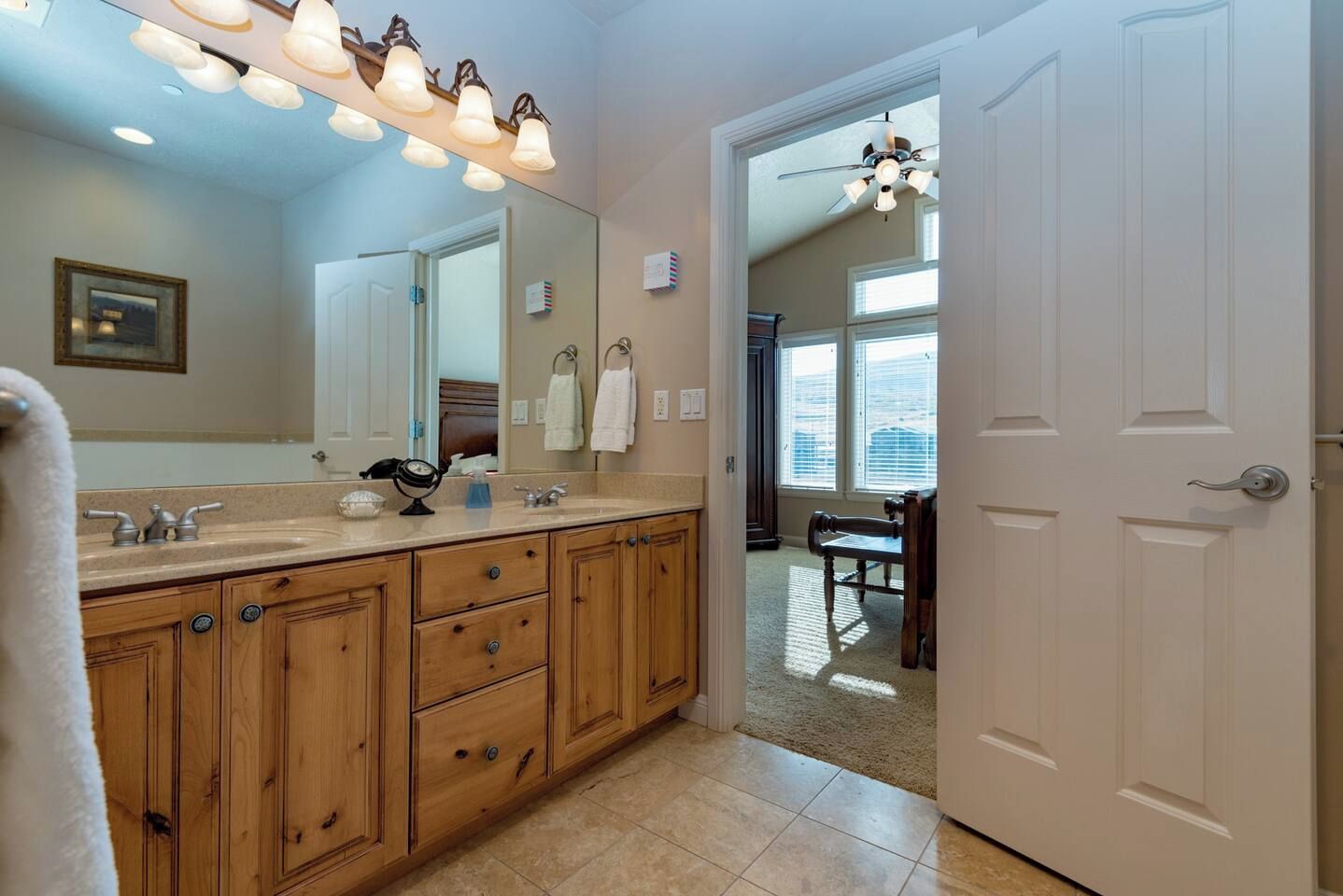 A bathroom with wooden cabinets, a large mirror, and a vanity with a sink. There is a towel rack with multiple towels and a clock on the vanity.