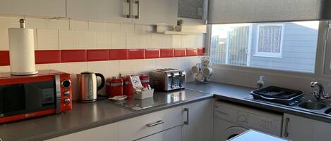 A kitchen with a microwave, toaster, kettle, and a dish rack.