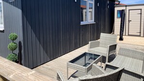 Ein dunkel gefärbtes Gebäude mit einer Terrasse, ausgestattet mit Korbmöbeln und einem Tisch mit Glasplatte.