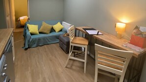 A compact living space with a sofa, a wooden table, a chair, and a kitchenette.