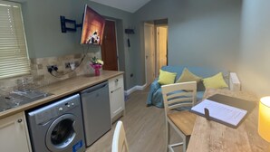 A compact kitchen with a washing machine, a dining area with a table and chairs, and a living space with a sofa.