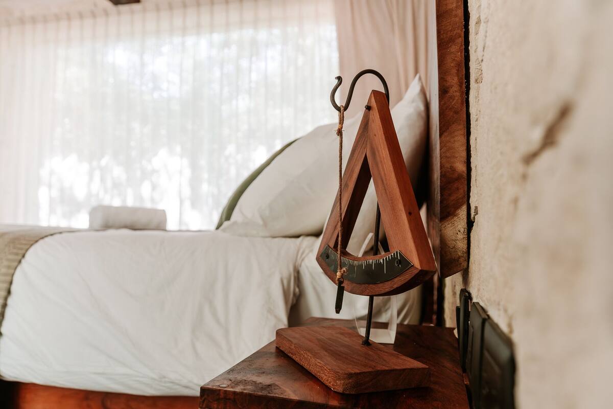 Estructura de cama de madera con cabecera, una mesita de noche de madera y una ventana con cortinas translúcidas.