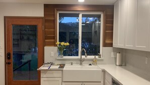 Una cocina moderna con armarios blancos, una puerta de madera, un ventanal con vistas y una alfombra estampada.