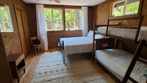 Una habitación de cabaña de madera con literas, una cama individual, una silla y una ventana con cortinas.