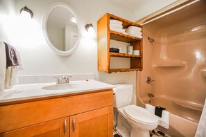 A bathroom with a white sink, wooden vanity, a toilet, a built-in shelf with towels, and a bathtub. - Neptune House (Block Island)