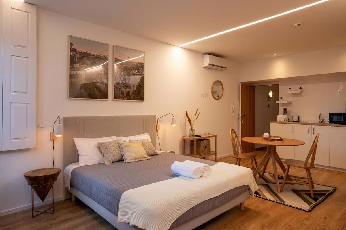 A modern bedroom with a large bed, bedside tables, a small round table, and a view of the kitchen.