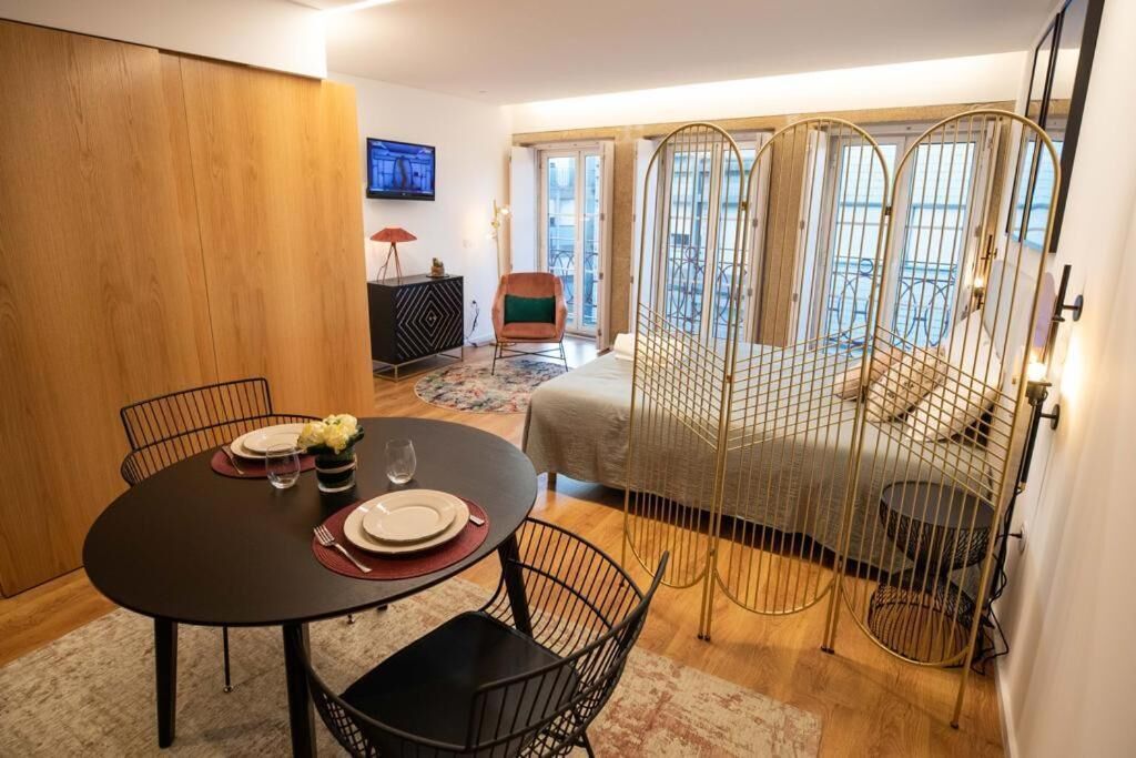 A compact bedroom with a bed, a dining table with chairs, a TV, and a balcony with a view.