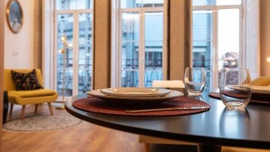 A dining area with a table set for two, near large windows with a view of buildings. - Lemago Poveiros Apartments (Porto)