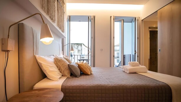 A bedroom with a large bed, a bedside table, and a lamp. - Lemago Poveiros Apartments (Porto)
